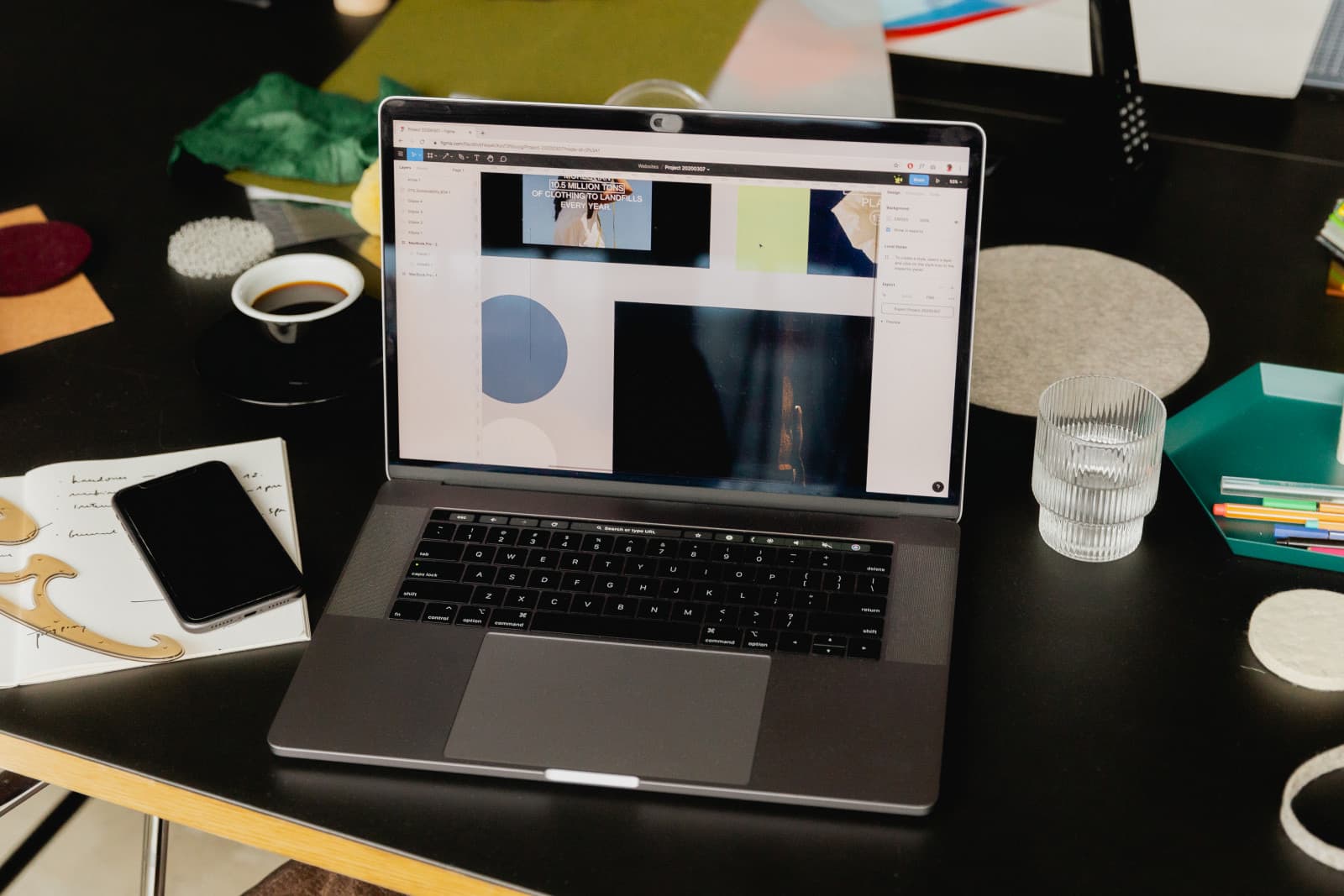 Portátil abierto con una app de diseño y mosaico de imágenes, junto a un cuaderno de notas a mano, teléfono, taza de café y vaso de agua