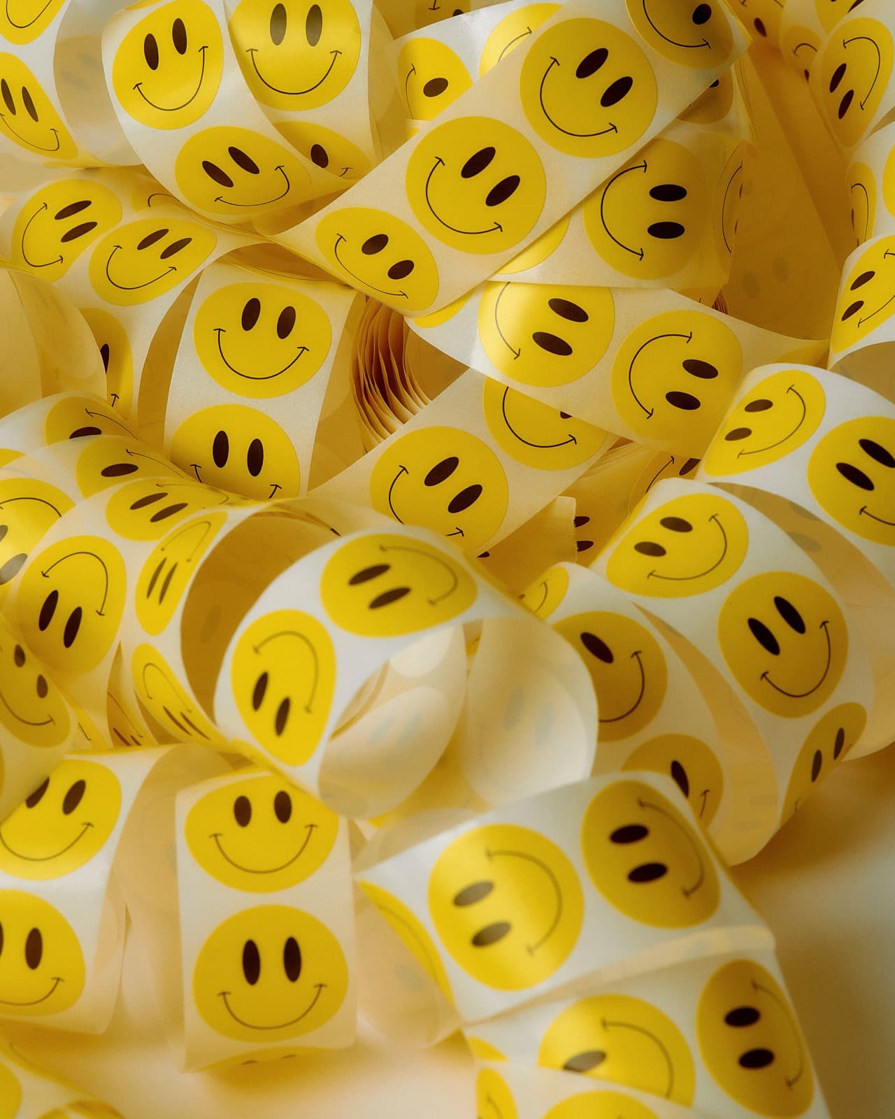 Tiras enroscadas de pegatinas redondas con caritas sonrientes, amontonadas sin orden unas sobre otras