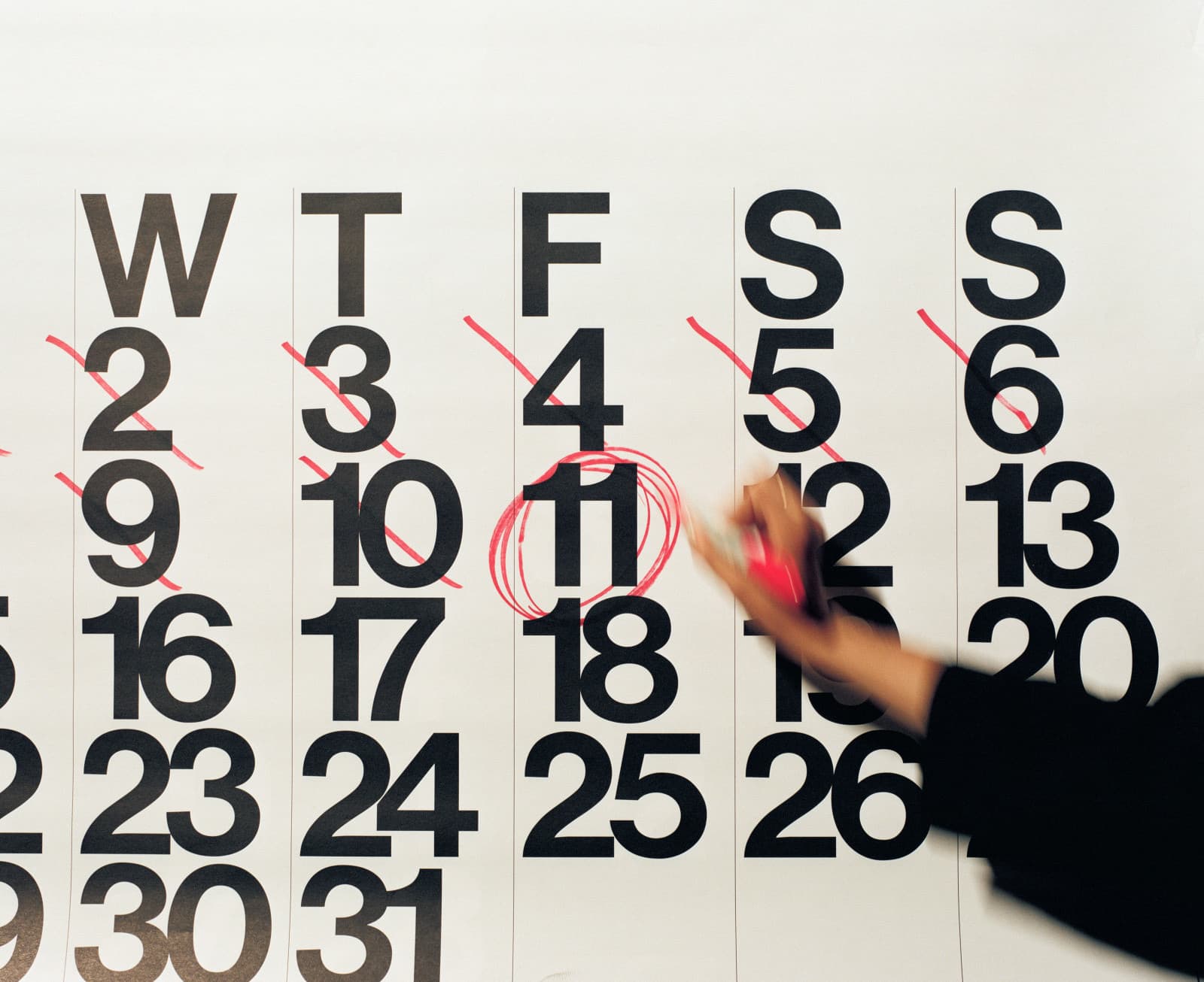 Mano con un rotulador rojo rodeando con un círculo el 11 en un gran calendario de pared, con los días anteriores tachados